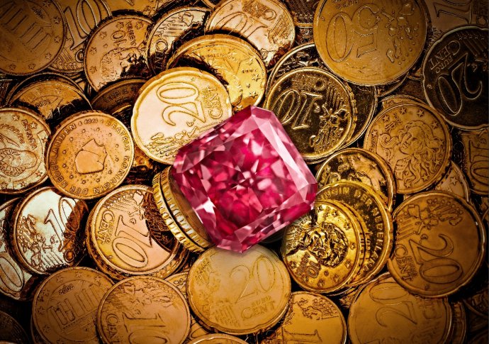 Pink gemstone on a pile of gold coins